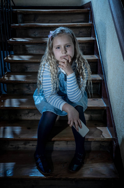 Sad depressed young girl victim of cyberbullying by mobile smart phone sitting on stairs feeling lonely, unhappy, hopeless and abused. Child bullied and harassed by text message by online stalker. - Zdjęcie, obraz