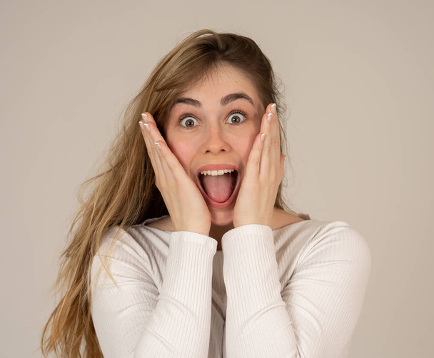 Beautiful young blonde teenager woman with happy face making surprised gestures looking and pointing at something shocking and good. Human facial expressions and emotions. Portrait with copy space. - Foto, imagen