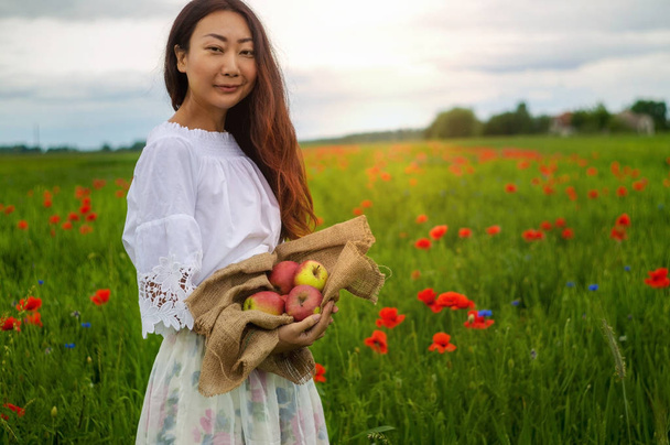 eine junge Frau mit einem Korb frisch gepflückter Äpfel auf einem Feld.  - Foto, Bild
