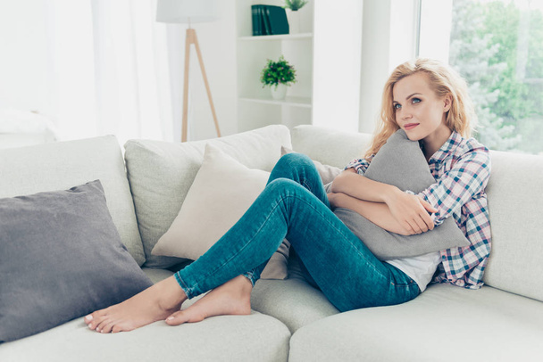 Portrait of her she nice-looking attractive lovely charming cute cheerful peaceful calm wavy-haired girl in checked shirt sitting on divan cuddling cushion at white light style interior living-room - Photo, Image