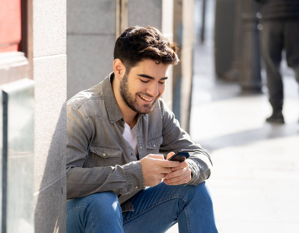 Fashion college man in his twenties happy checking blog or chatting on the internet with friends on smart mobile phone app in european outdoors city. In communication technology and travel Europe. - Foto, imagen