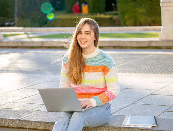 Pretty young cheerful teenager woman working or studying on laptop computer sitting happy and on stairs in city outdoors urban background. In student lifestyle Online education and Technology concept. - Фото, зображення