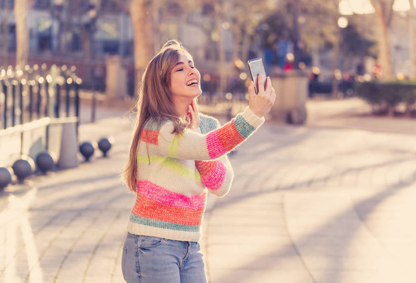 Pretty teenager girl taking selfie happy and excited in the city. Young student woman recording video of herself blogging outdoors In Millennial generation Connections Technology and Online trends. - Photo, image