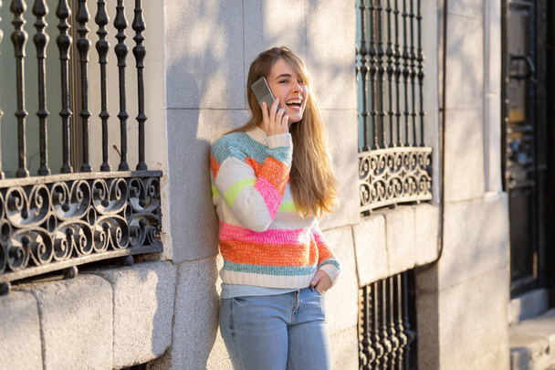 Pretty happy teenager woman talking on mobile smart phone outside city street. Beautiful stylish college student wearing fashion clothes feeling relaxed and free. Lifestyle, beauty and technology use. - Zdjęcie, obraz