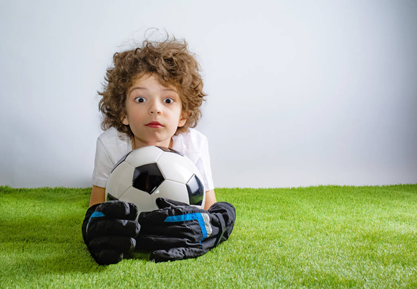 Kid - soccer champion. Boy goalkeeper in football sportswear with ball on gray background. Sport concept. Copy space. - Foto, imagen