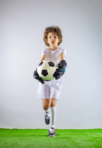 Kid - soccer champion. Boy goalkeeper in football sportswear with ball on gray background. Sport concept. Copy space. - Φωτογραφία, εικόνα