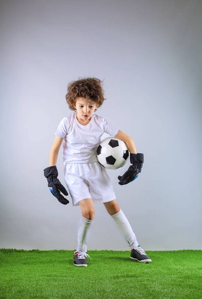 Kid - soccer champion. Boy goalkeeper in football sportswear with ball on gray background. Sport concept. Copy space. - Fotoğraf, Görsel