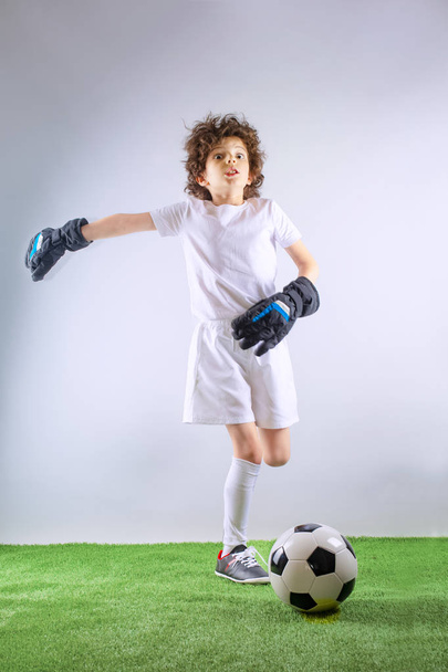 Kid - soccer champion. Boy goalkeeper in football sportswear with ball on gray background. Sport concept. Copy space. - Foto, afbeelding