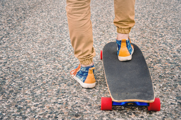 Close-up of male legs in rag sneakers on a longboard on the background of asphalt at sunset. Big skateboard with man legs. Youth leisure concept - Fotó, kép