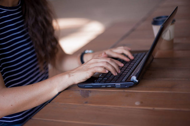Nette jonge vrouwelijke handen zonder manicure, met grote polshorloges, werken op een laptop, staande op een houten tafel. - Foto, afbeelding