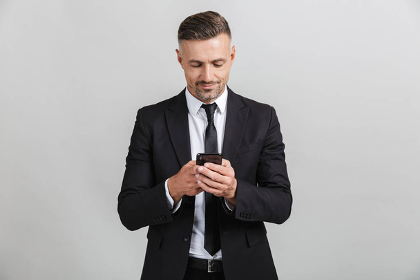 Image of successful handsome businessman in formal suit typing on cellphone - Zdjęcie, obraz