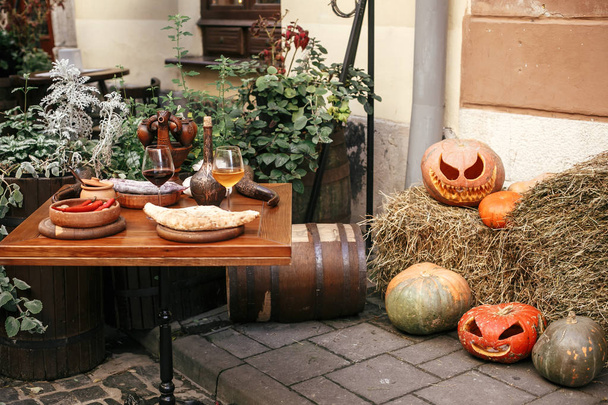 Тыквы со страшными лицами на сене за столом кафе, праздничные украшения
 - Фото, изображение