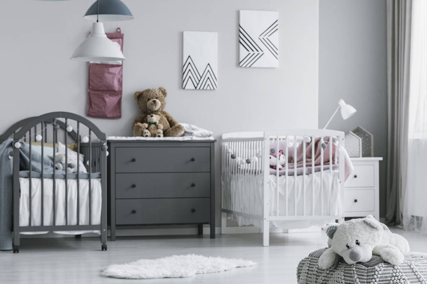 Real photo of a cute, white teddy bear on a pouf in a bright kid bedroom interior with twin beds - Fotó, kép