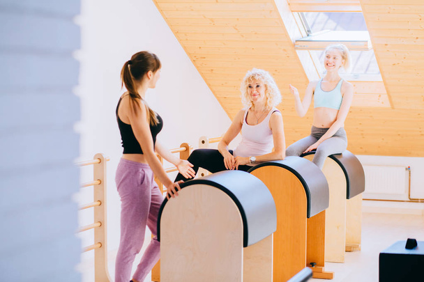 Trainerin und zwei Klienten diskutieren ihre Fortschritte im Pilates-Studio. - Foto, Bild