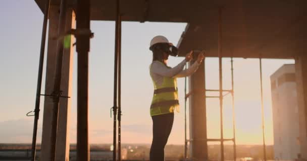 Inspektor ženy ve VR a přilbě kontroluje postup výstavby mrakodrapu, který při západu slunce vizualizuje plán stavby. - Záběry, video