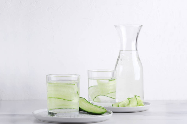 Two glasses and bottle of healthy cucumber water on the plates. kitchen white table - 写真・画像