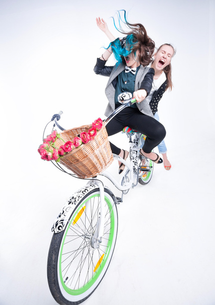 dos chicas montando en bicicleta haciendo caras graciosas - aisladas sobre fondo azulado
 - Foto, imagen