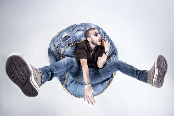 Funny crazy man dressed in jeans and sneakers standing on denim beanbag - Foto, Imagem