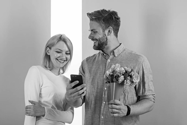 Romantic concept. Couple in love interested by phone. Guy with phone and bouquet of flowers, pastel pink and green background. Man shows photo on smartphone to girl, sweet memories of their relations - Foto, Imagem