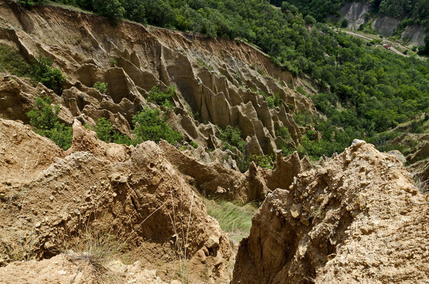 Fragmentti kuuluisa Stobs Pyramidit epätavallisen muotoinen punainen ja keltainen kallio kokoonpanoissa, vihreä pensaita ja puita ympärillä, länsiosassa Rila vuori, Kyustendil alue, Bulgaria, Eurooppa
  - Valokuva, kuva