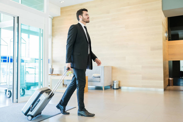 Magabiztos középső felnőtt igazgató gyaloglás-ban előcsarnok rövid idő húz bőrönde-on szálloda - Fotó, kép