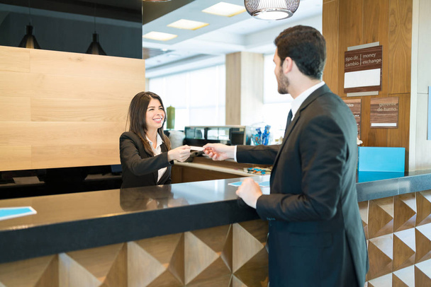 Escriturário sorrindo do hotel que recebe o pagamento através do cartão de crédito do homem de negócios para a reserva no balcão no lobby
 - Foto, Imagem