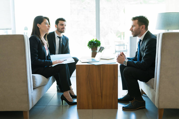Zelfverzekerde verkoper legt business plan uit aan mannelijke en vrouwelijke ondernemers tijdens een ontmoeting in het Hotel - Foto, afbeelding
