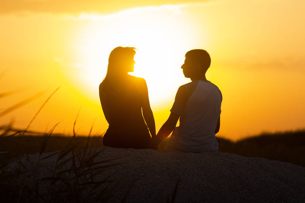 silhouette of a loving couple at sunset sitting on sand on the beach, the figure of a man and a woman in love, a romantic scene in nature, a family vacation, summer rest - Photo, Image