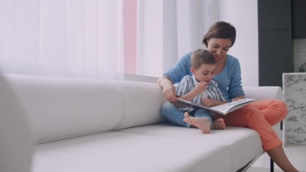 Szerető anya a fiát, hogy olvassa el a gazdaság könyv beszél a kanapén, otthon oktatási. - Felvétel, videó
