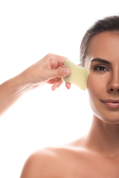 cropped view of nude young woman using gua sha scraper isolated on white - Zdjęcie, obraz