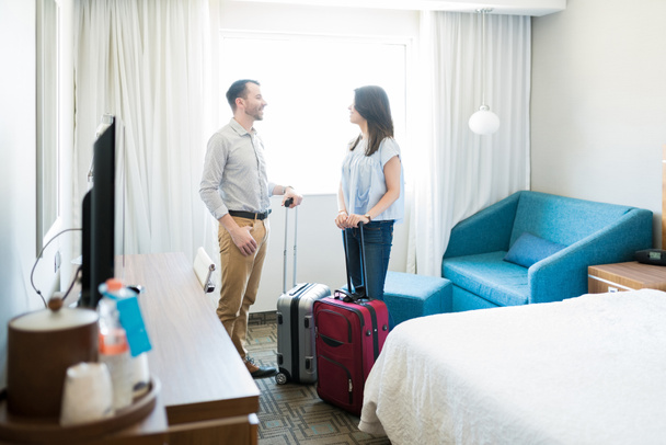 Pareja hispana en luna de miel de pie con equipaje mientras camina en la habitación en el hotel
 - Foto, Imagen