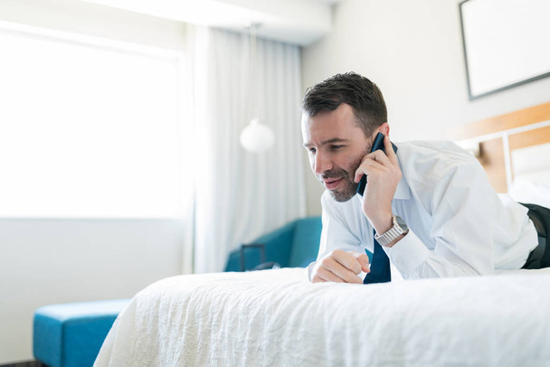 Entrepreneur masculin adulte moyen parlant sur un téléphone portable tout en se reposant sur le lit dans la chambre d'hôtel
 - Photo, image