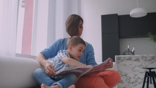 Moeder en zoon lezen boeken. Gelukkige jonge moeder en zoon lezen boeken op de Bank thuis. - Video
