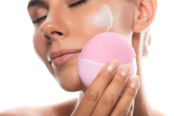 cropped view of nude young woman with cream on face using facial cleansing brush isolated on white - Φωτογραφία, εικόνα