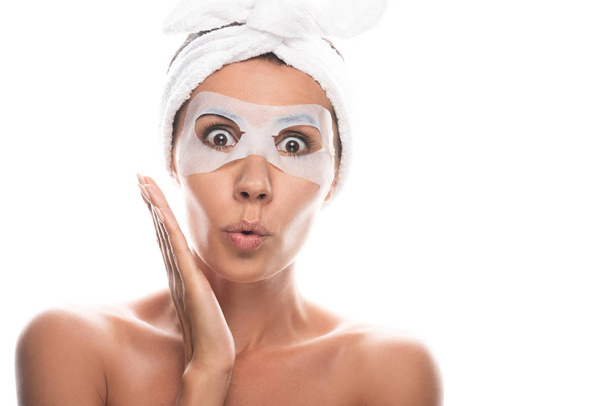 фронтальный вид шокированной обнаженной девушки в косметической ленте волос с маской для лица, изолированной на белом
 - Фото, изображение
