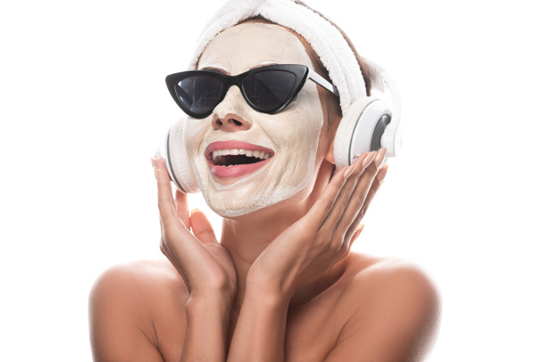 mulher nua em banda de cabelo cosmético e óculos de sol com máscara facial ouvir música em fones de ouvido isolados em branco
 - Foto, Imagem