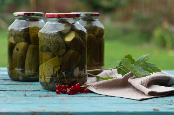 Homemade canned cucumbers in a jars on a blue wooden background, harvesting vegetables, pickles. Fresh and pickled cucumbers, homemade preserved vegetables - Photo, Image