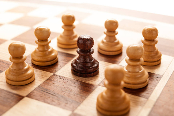 Μαύρο πιόνι στο σκάκι, περιτριγυρισμένος από άσπρα πιόνια σκακιού - Φωτογραφία, εικόνα