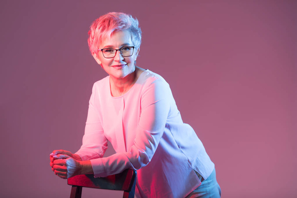 beautiful stylish woman in age, with glasses with a short haircut on a pink background - Foto, imagen