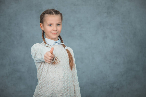 A happy and proud schoolgirl is gesturing thumb up is isolated on grey background. - Foto, afbeelding
