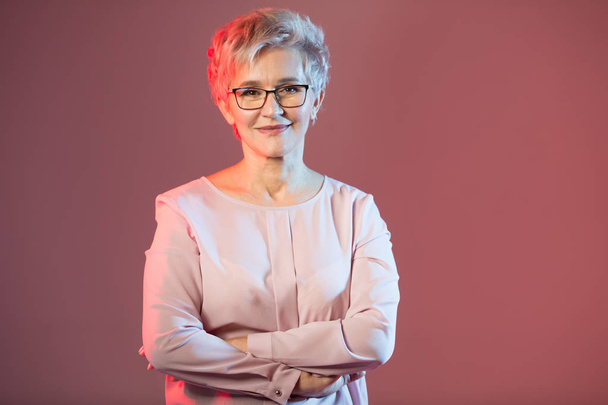 beautiful stylish woman in age, with glasses with a short haircut on a pink background - Foto, immagini