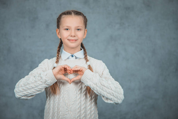 Young beautiful smart student girl shows heart and is isolated on grey background - Zdjęcie, obraz