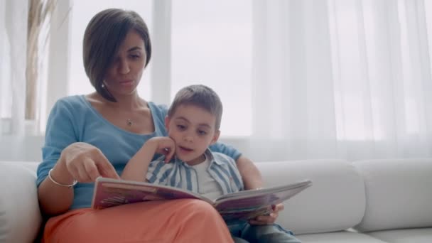 Happy mother and child son reading book laughing in bed. Happy family mother and child son reading holding book lying in bed, smiling mom baby sitter. - Footage, Video