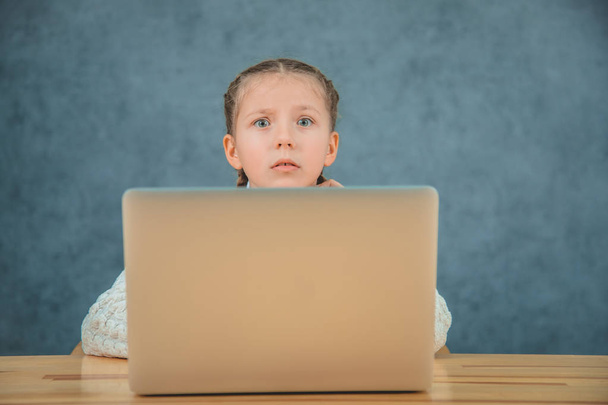 Cute elementary student feeling sad and confusing while sitting in front of her laptop sitting in front of grey laptop. - Foto, afbeelding