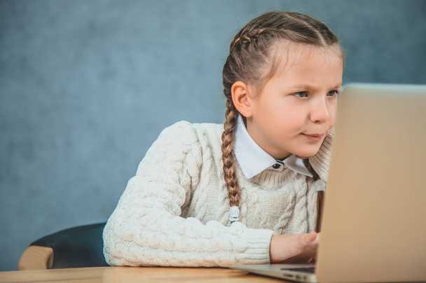 Cute little girl with braids is using laptop in looking at it with curiousity. - Photo, Image