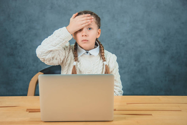Schattige kleine charmante blonde meid zit in de voorkant een laptop. Meisje vergat haar huiswerk en raakt haar hoofd met een rechterhand. - Foto, afbeelding