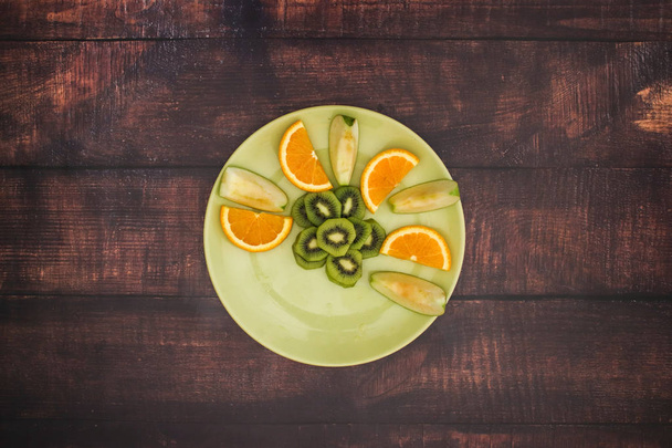 Green plate with fresh fruit salad on the wooden table  - Photo, Image