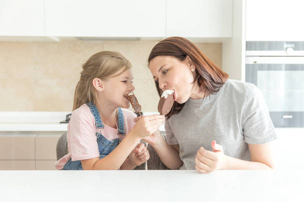 Mère avec fille dans la cuisine manger de la crème glacée. Bonnes relations parent-enfant. Concept de famille heureuse
 - Photo, image