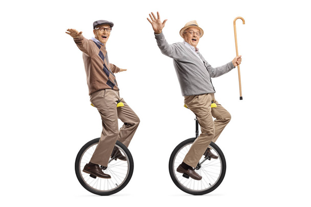Two cheerful senior men riding unicycles and looking at the came - Zdjęcie, obraz