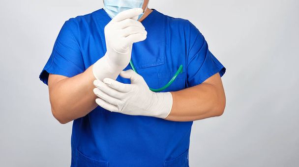 male doctor in blue uniform puts on his hands white sterile late - 写真・画像